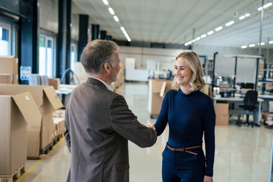 Happy businesswoman handshaking with colleague at warehouse