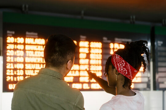 Young woman talking to friend and pointing at departure board