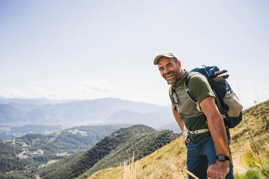 Cheerful mature man with backpack standing on mountain