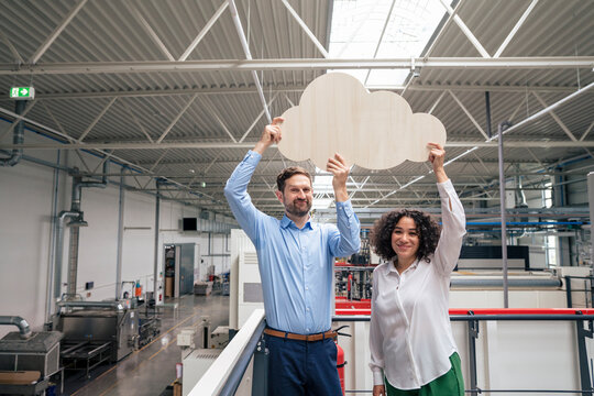 Smiling businessman and businesswoman holding cloud shaped cut out in industry