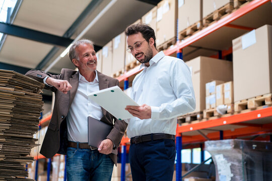 Happy senior businessman with colleague discussing over document at warehouse