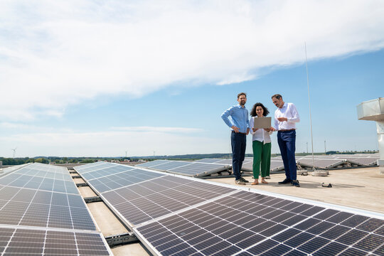 Businesswoman with colleagues discussing over laptop by solar panels