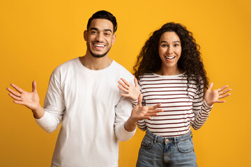 Portrait Of Joyful Arab Couple Spreading Hands With Excitement Over Yellow Background