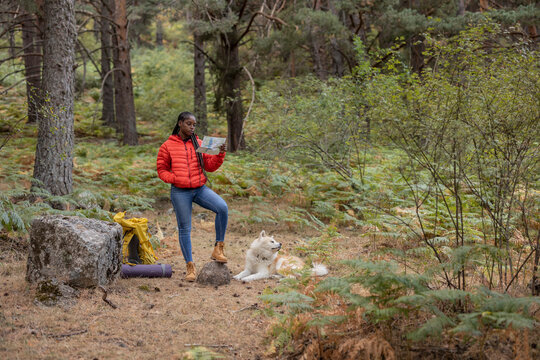 Young woman reading map with dog sitting in forest