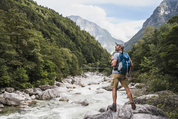 Mature man with backpack standing on rock by river