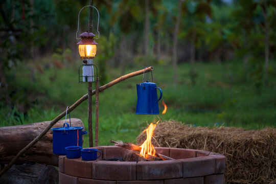 Enamel Coffee Maker Set On The Stove With Firewood And Ancient Gas Lamps In The Middle Of The Forest Camping In The Evening