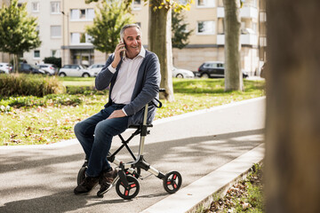 Happy senior man talking on mobile phone sitting on mobility walker