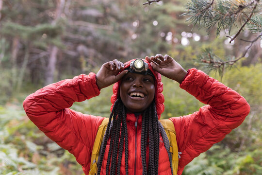 Happy woman wearing flashlight on forehead standing in forest