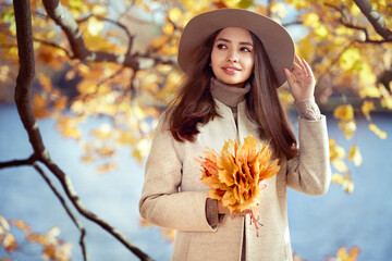 Autumn portrait of a beautiful happy smiling woman with yellow maple leaves in a white coat in the...