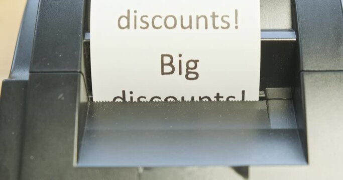 Receipt printer prints text: big discounts. Close-up, front view, increase font. Concept of promotions, sales in stores.
