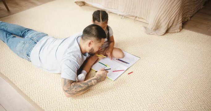 Father and daughter lying on floor draw picture together
