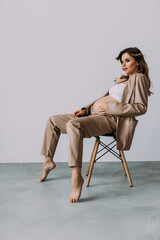 Pregnant young woman sitting on a chair on a white background