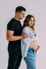 Fototapeta premium Happy Couple Expecting Baby. Beautiful Young Pregnant Woman and Her Husband Sitting Together and Caressing Her Pregnant Belly