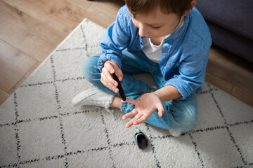 Little diabetic boy taking blood sample with lancet pen at home. World Diabetes Day