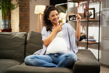 Obraz premium Pregnant woman with ultrasound photo. Beautiful pregnant woman enjoy at home.