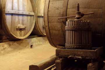 Ancient underground wine cellar with wooden oak casks for wine aging and screw press in foreground