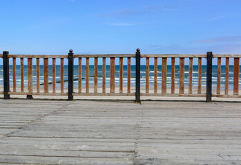 The pier is fenced in front and rear with a orange, wood fence. In the background there is a blue sea and a bright sky.