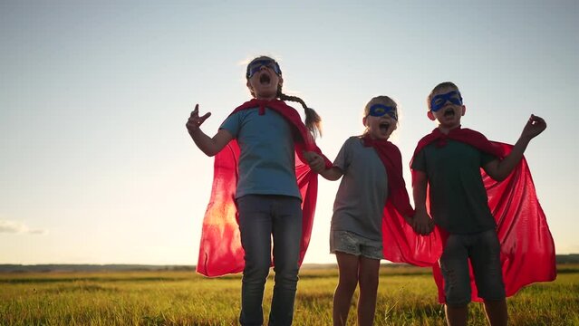 team superhero. a group of children are running dream across the field in a superhero costume with a silhouette of a red cape at sunset. the concept of a happy family childhood. teamwork superhero