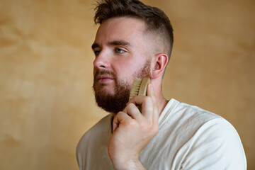 Portrait brutal handsome bearded man with blue eyes holding comb,  natural brush, male personal...
