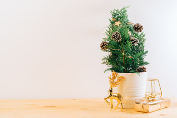 Creative natural miniature Christmas tree in pot on wooden table with gift boxes and white background. Xmas greeting card with copy space. Happy New Year