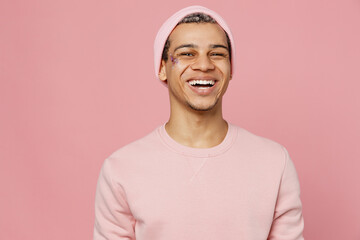 Young smiling fun positive cheerful trendy handsome fun gay man wear sweatshirt hat looking camera isolated on plain pastel light pink color background studio portrait Lifestyle lgbtq pride concept.