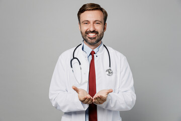 Male doctor happy man wears white medical gown suit work in hospital hold hands show empty palms offer something isolated on plain grey color background studio portrait. Healthcare medicine concept.