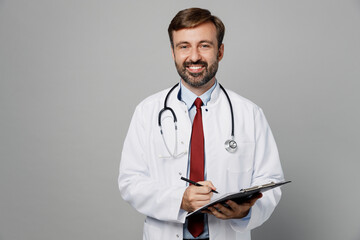 Male doctor smiling fun happy man wear white medical gown suit work in hospital hold clipboard write down in paper documents isolated on plain grey color background studio Healthcare medicine concept