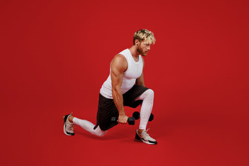 Full size side view young strong sporty toned sportsman man wearing white clothes spend time in home gym hold dumbbells do lunge squats isolated on plain red background Workout sport fit body concept.
