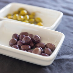 black olives and green olives in white saucers on a gray tablecloth on the table. Horizontal frame. Place for text