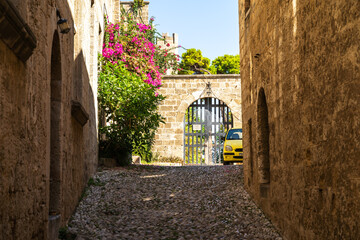 A yellow car on a stone street in the old town peeks out from around the corner of an old stone building