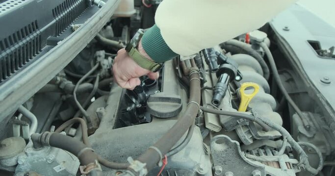 Men's hands unscrew the bolts of the car's candle box under the hood with a ratchet wrench. Close-up, changing spark plugs in a car.