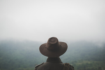 Freedom traveler man in hat carrying a backpack stands at the top of a mountain on a foggy...
