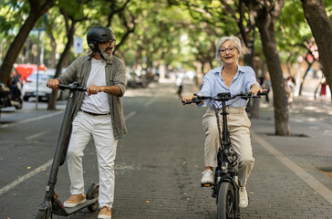 senior tourists riding electric bikes and electric scooters around town © PintoArt
