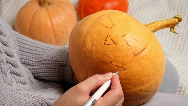 oman Preparing Halloween Pumpkin. Hands drawing and carves a scary Halloween Pumpkin at Home interior. Making Jack Lantern Decor for Halloween. Preparation for Celebration. Festive Jack Face. 4K