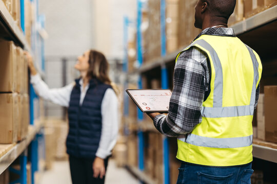 Two warehouse workers taking stock using warehouse management software. Logistics workers using a digital tablet while doing inventory management.
