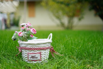 White wicker basket with decorative pink roses stands on green grass in the middle of the garden. Copy space