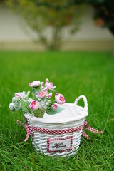 White wicker basket with decorative pink roses stands on green grass in the middle of the garden. Copy space