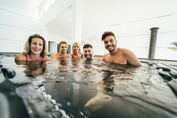Group of friends having fun relaxing in hot tub inside private village party - Main focus on right man face
