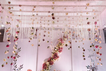 Festive table, arch, stand, garland decorated with a composition of pink flowers and greenery, candles in the banquet hall. Table newlyweds in the banquet area at the wedding party.