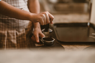 Barista using a tamper to press ground coffee into a portafilter. Coffee maker concept..