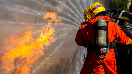 Obraz premium Asian firefighter on duty firefighting, Asian fireman spraying high pressure water, Fireman in fire fighting equipment uniform spray water from hose for fire fighting.