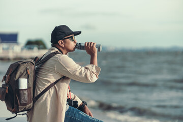 Obraz premium A backpacker sitting to sea watching the sunset and drank his thirst. backpacker concept.
