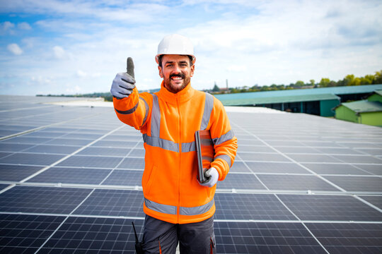 Portrait of professional solar company worker holding thumbs up on the rooftop after successful solar panels installation.