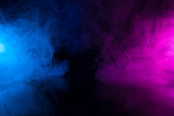 Clouds of colorful smoke in blue and purple neon light swirling on black table background with...