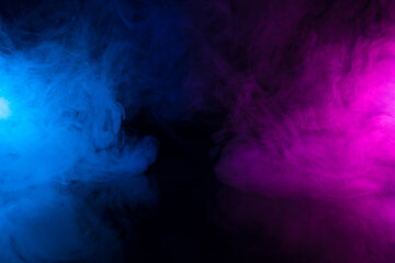 Clouds of colorful smoke in blue and purple neon light swirling on black table background with reflection