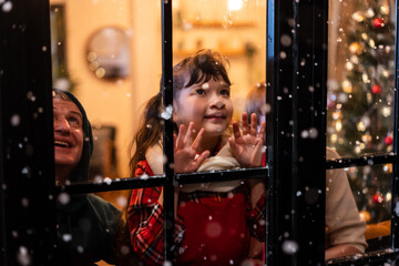 Adorable child look through the window and admiring first snow flakes. 