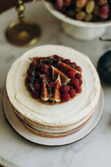 biscuit cake with white cream decorated with raspberries and sliced figs. decorated cake on a white table. birthday cake top view	
