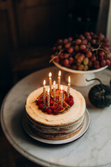birthday cake with burning candles on top. biscuit cake with white cream decorated with raspberries and sliced figs. decorated cake on white table