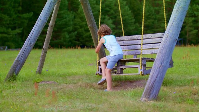 A small child runs to the vacated swing. Summer outdoor games. The boy swings on a wooden swing.