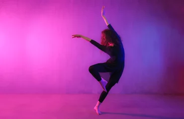 Poster Modern dance girl dancer dancing in neon light doing gymnastic exercises in studio, copy space. © Halfpoint